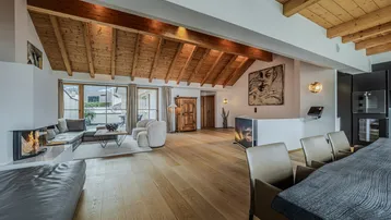 Geräumiger offener Wohn- und Essbereich mit Holzbalkendecke, Kamin und Zugang zu einem Balkon.