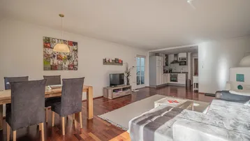 Helles, offenes Wohn-Esszimmer mit Holzboden und integrierter Küche, ideal für geselliges Beisammensein.