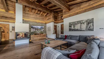 Geräumiges Wohnzimmer mit modernem Kamin, bequemer Sitzecke und beeindruckender Holzbalkendecke.