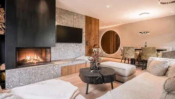 Gemütlicher Wohn-Essbereich im modernen alpinen Stil mit Kamin und Holzelementen.
