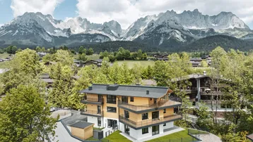 Modernes Gebäude mit Holzfassade und Bergblick unter bewölktem Himmel in alpiner Umgebung.