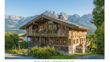 Traditionelles Holzchalet mit Blumenkästen und beeindruckendem Bergblick unter blauem Himmel.