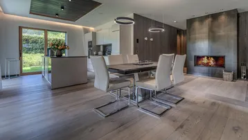 Moderner Essbereich mit Holzboden, Kamin und offener Küche im Hintergrund.