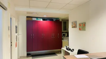 Empfangsbereich oder Flur in einem Bürogebäude mit roten Schränken, einem Schreibtisch und Fliesenboden.