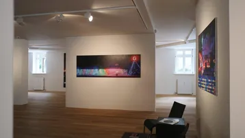 Heller, offener Raum mit Holzboden, weißen Wänden und Kunstwerken, beleuchtet durch moderne Deckenspots.