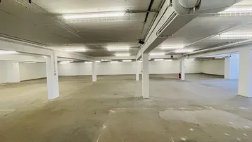 Geräumige Tiefgarage oder Lagerfläche mit Betonboden, vielen Stützen und sichtbaren Leitungen an der Decke.