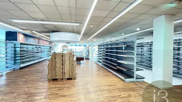 Großer Gewerberaum mit Holzfußboden und leeren Regalen, ausgestattet mit moderner Deckenbeleuchtung.