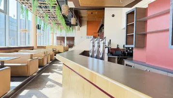 Geräumiger Restaurantbereich mit langer Theke, Zapfanlage und großen Fenstern, die viel Tageslicht hereinlassen.