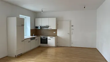 Helle, offene Küche mit weißen Schränken, Holzboden und integrierten Geräten in einem Wohnbereich.
