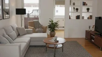 Gemütliches Wohnzimmer mit Sofa, Teppich, Holzboden und Zugang zum Balkon.