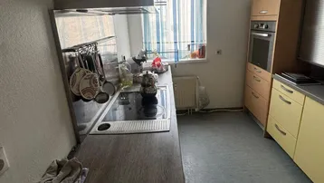 Funktionale Küche mit Kochfeld, Dunstabzugshaube und hellen Schränken, ausgestattet für den täglichen Gebrauch.