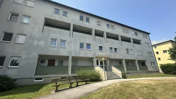 Mehrstöckiges Wohngebäude mit mehreren Balkonen und einer Treppe zum Eingangsbereich.
