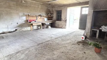 Geräumiger Werkstattbereich mit Betonboden, Arbeitstisch und einem großen Kamin oder Ofen.