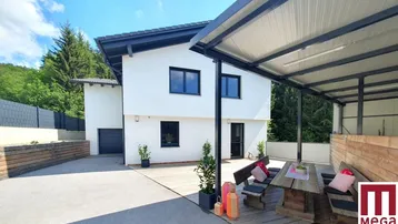 Modernes Einfamilienhaus mit überdachter Terrasse und Holzboden, umgeben von viel Grün.