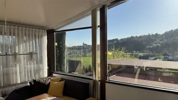 Heller Wintergarten mit großen Fenstern und weitem Blick auf die grüne Landschaft.