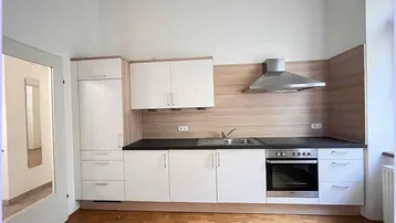 Helle Einbauküche mit weißen Schränken, dunkler Arbeitsplatte und Holzparkettboden.