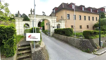 Historisches Gebäude mit imposantem Torbogen, umgeben von Grünflächen und einer Zufahrt.