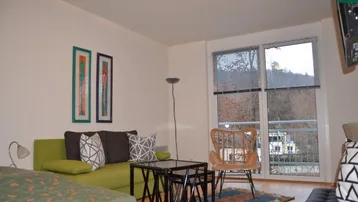 Helles Wohnzimmer mit Sofa, Sessel und Zugang zu einem Balkon mit Blick ins Grüne.