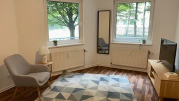 Helles Wohnzimmer mit Laminatboden, modernem Teppich und Blick ins Grüne durch große Fenster.