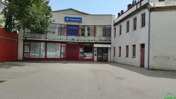 Außenansicht von zwei Gebäuden mit einem asphaltierten Vorplatz, der als Parkplatz dient und roten Akzenten.