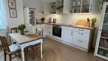 Helle Küche mit Holzboden, weißer Einbauküche und Essbereich mit Korblampe.