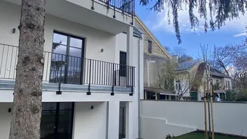 Moderne Gebäudefassade mit Balkonen und einem gepflegten Gartenbereich mit Treppen.