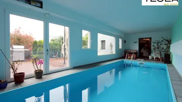 Heller Innenpoolbereich mit großen Fenstern, die den Blick auf die Terrasse und den Garten freigeben.