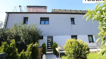 Moderne Hausfassade mit Eingangsbereich, umgeben von gepflegten Büschen und Solaranlagen auf dem Dach.