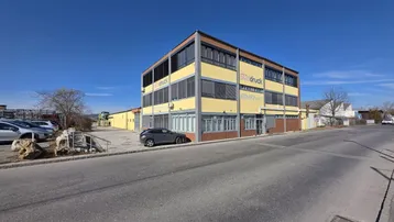Modernes Geschäftsgebäude mit gelber Fassade und großen Fenstern unter blauem Himmel.