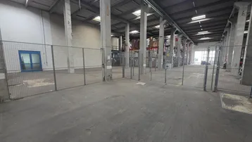 Geräumige Lagerhalle mit Betonboden, hohen Decken und Oberlichtern, durch Gitterzäune unterteilt.