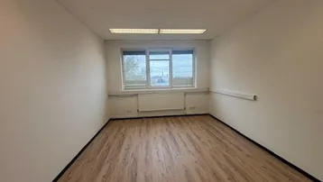 Leeres Büro mit Laminatboden, weißen Wänden und einem Fenster mit Blick nach draußen.