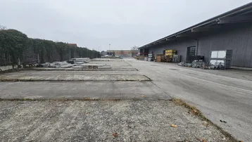 Großer Außenbereich mit asphaltierter Fläche neben einem Industriegebäude unter bewölktem Himmel.