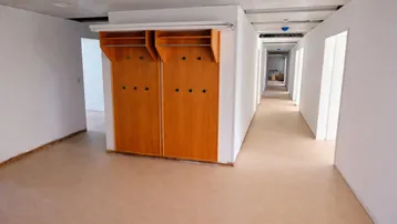 Langer Flur mit hellen Wänden, beigem Boden und integrierten Garderobenschränken aus Holz.