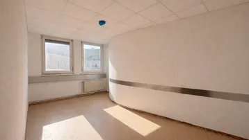 Leerer Raum mit zwei Fenstern, hellem Boden und einer gebogenen Wand mit Metalleiste.