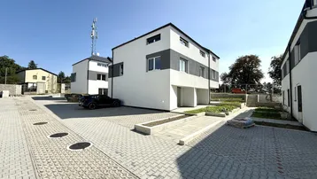 Moderne Reihenhäuser mit weiß-grauer Fassade und gepflasterten Parkplätzen unter blauem Himmel.