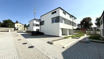 Moderne Reihenhäuser in einer neuen Wohnsiedlung mit gepflasterten Parkplätzen unter blauem Himmel.