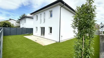 Modernes Einfamilienhaus mit frisch angelegtem Rasen und kleiner Terrasse unter bewölktem Himmel.
