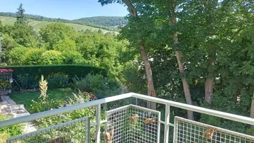 Blick vom Balkon auf den grünen Garten und die umliegende Hügellandschaft mit Weinbergen.