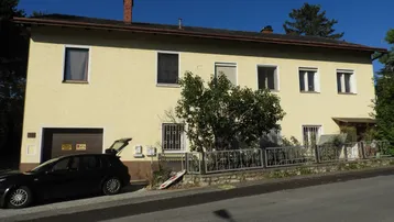 Gelbe Fassade eines Wohnhauses mit Garagentor und geparktem Auto davor an einem sonnigen Tag.