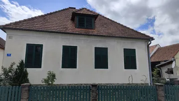 Traditionelles Einfamilienhaus mit weißer Fassade, roten Dachziegeln und grünen Fensterläden.