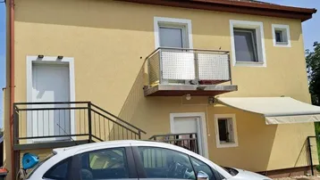 Gelbes Einfamilienhaus mit rotem Ziegeldach, kleinem Balkon und gepflasterter Auffahrt.