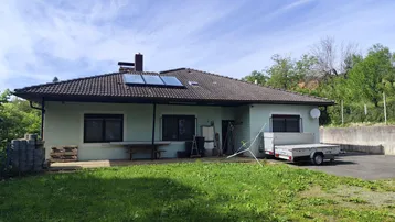 Hausfassade mit Solarpaneelen auf dem Dach und einem grünen Vorgarten.