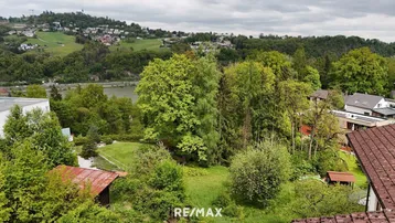 Weitläufiger Blick über grüne Hügel, Bäume und einen Fluss in der Ferne mit umliegenden Häusern.