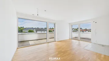Helles, leeres Wohnzimmer mit Parkettboden und großzügigem Zugang zu einem Balkon.