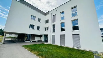 Moderne Architektur eines Mehrfamilienhauses mit weißer Fassade und gepflegter Grünfläche.