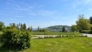 Weitläufige grüne Landschaft mit Hügeln und einem Feldweg unter blauem Himmel.