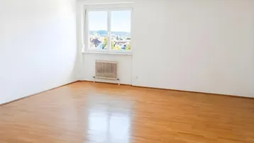 Helles, leeres Zimmer mit Parkettboden und einem Fenster, das einen weiten Blick über die Stadt bietet.