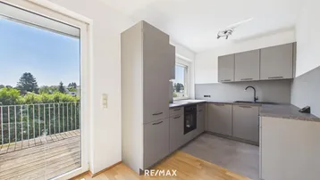 Moderne Küchenzeile in Grau mit integrierten Geräten und Balkonzugang.