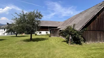 Großes Grundstück mit weitläufiger Rasenfläche und traditionellem Bauernhaus unter blauem Himmel.