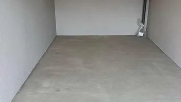 Leerer Raum mit Betonboden und hellgrauen Wänden, ausgestattet mit Decken- und Wandleuchten.